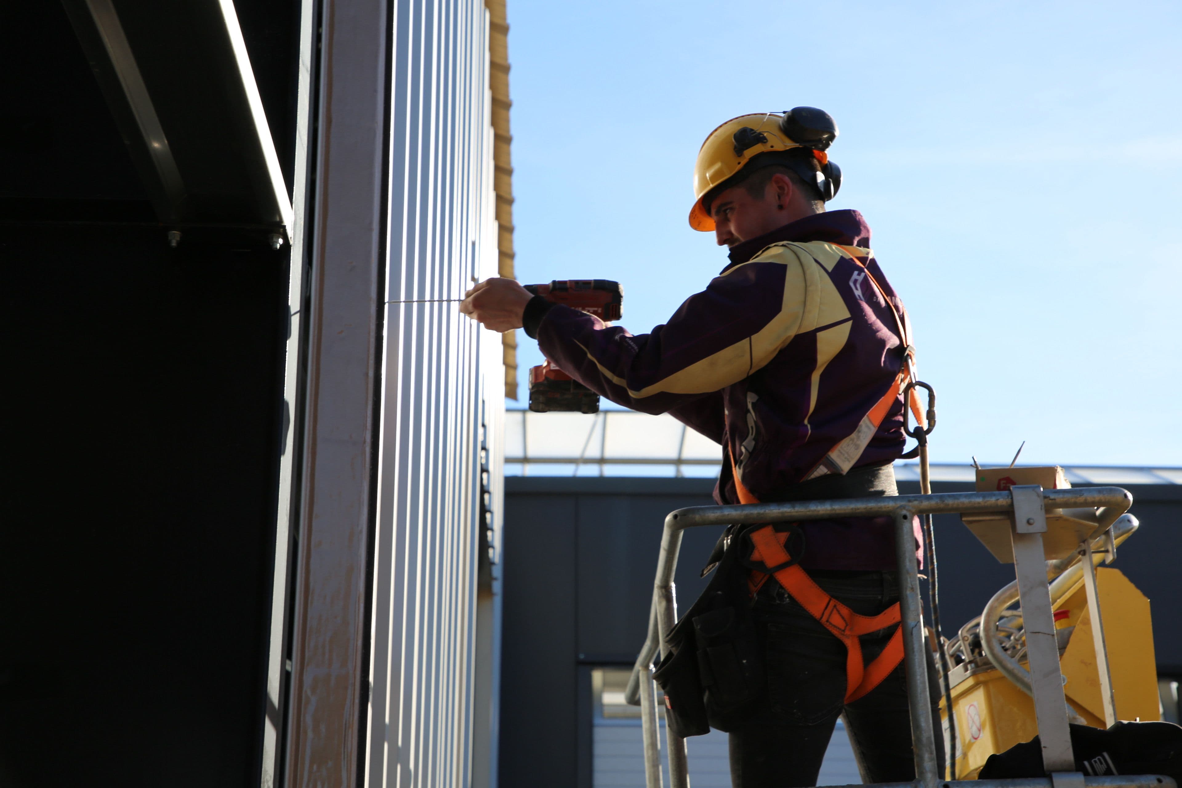 Monteur plaatst geïsoleerde wandpanelen aan buitengevel van bedrijfshal