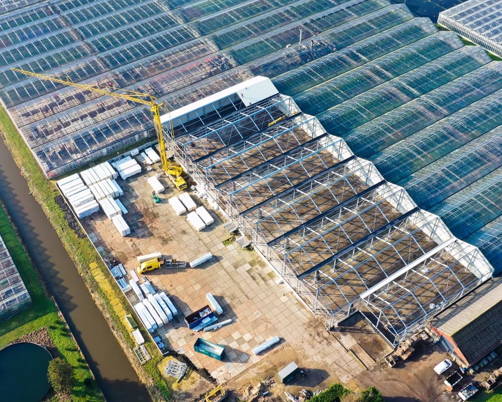 Bouwfase van bedrijfshallen Mijdrecht naast kassencomplex met dakmontage