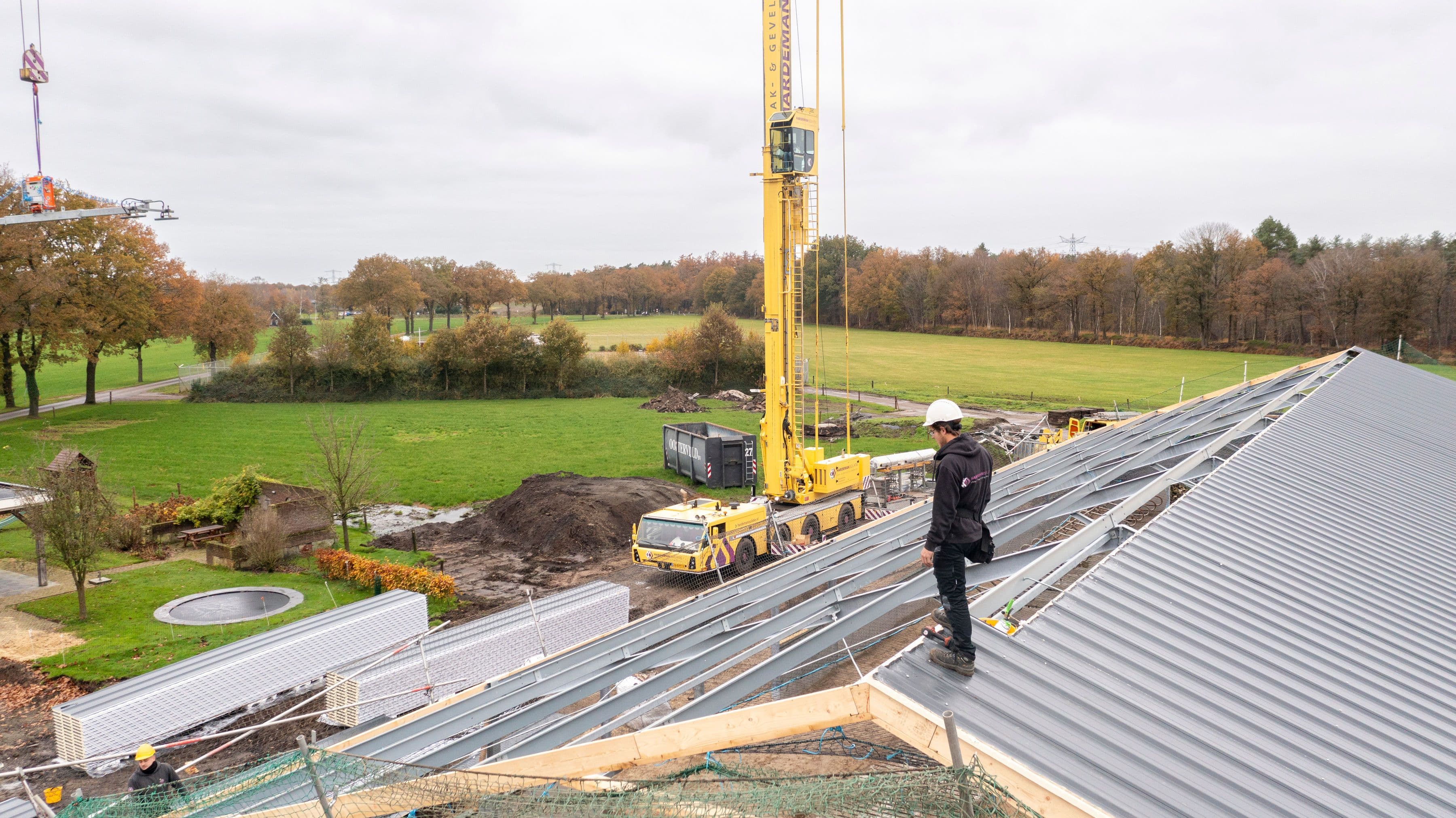 Man die op een dak staat die gerenoveerd wordt met een kraan ernaast