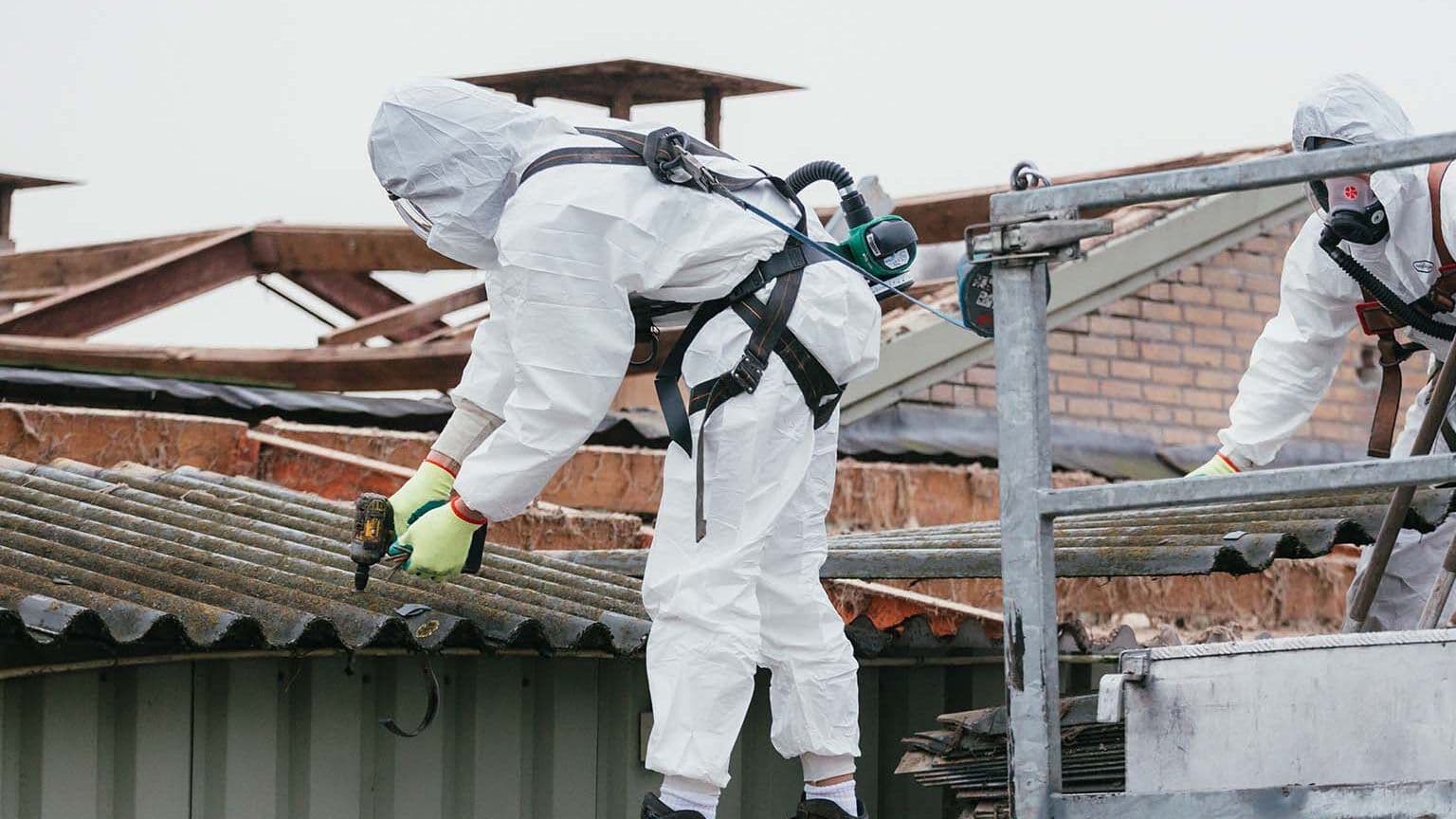 Medewerkers verwijderen asbestplaten van een dak in beschermende kleding