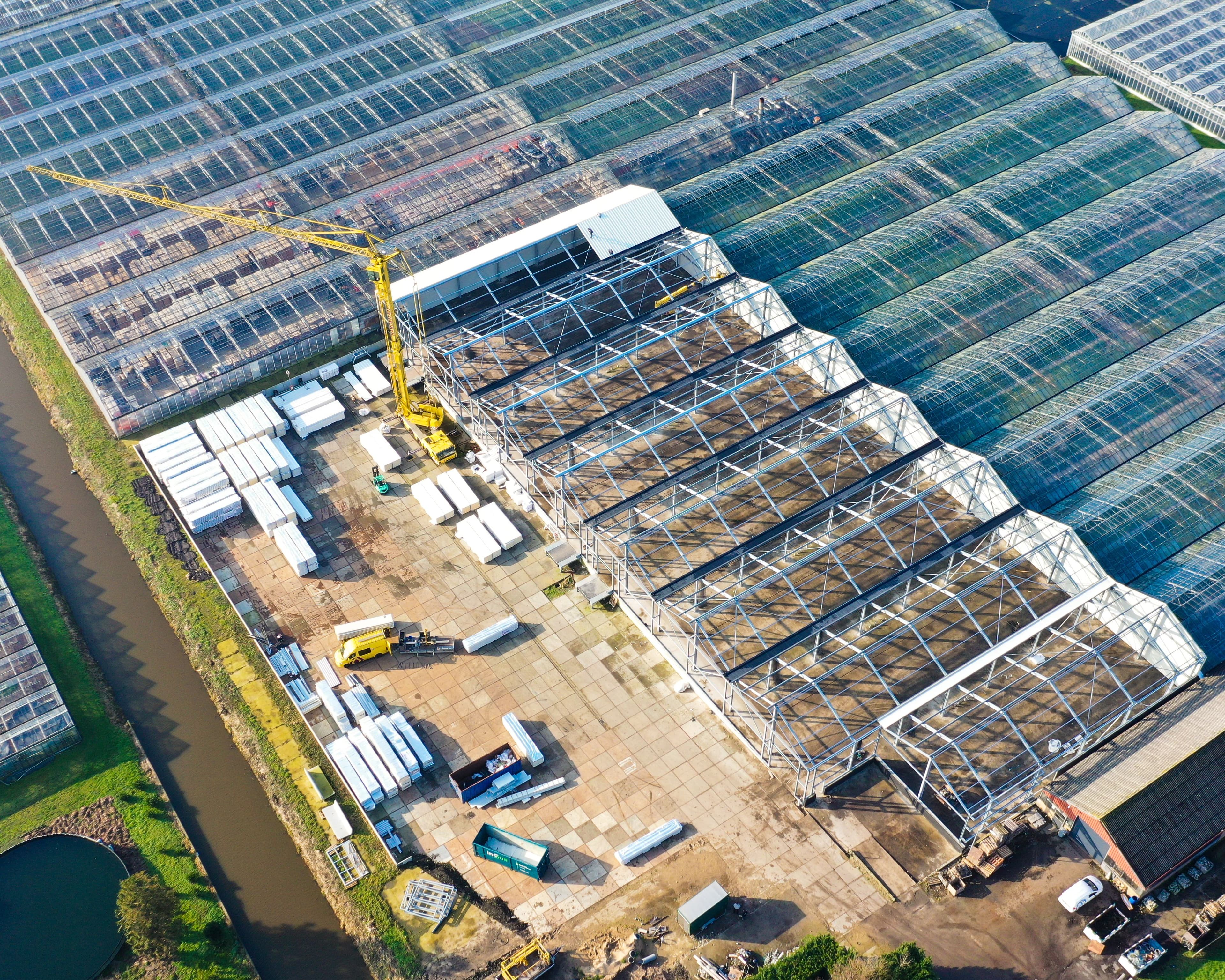 Bouwfase van bedrijfshallen Mijdrecht naast kassencomplex met dakmontage